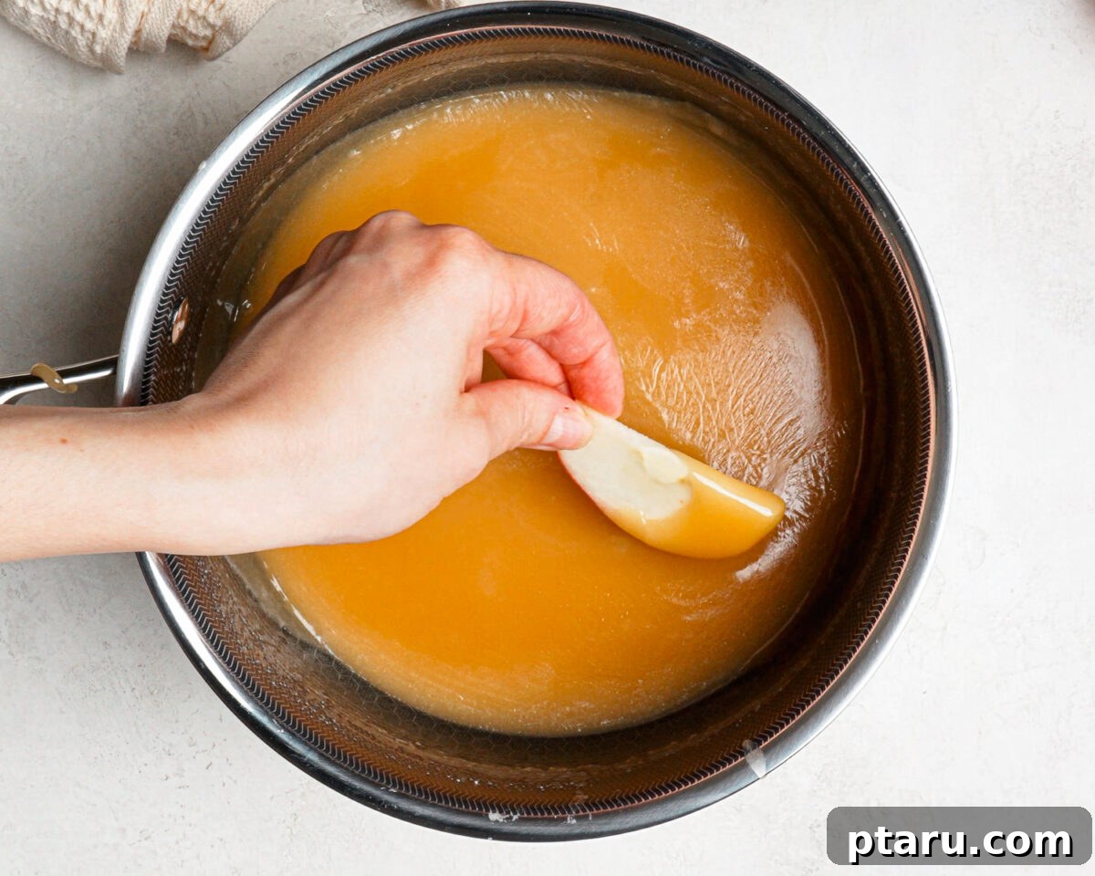 Caramel Apple Slices with Homemade Caramel Sauce 9 Dipping an apple slice into homemade caramel in a saucepan.