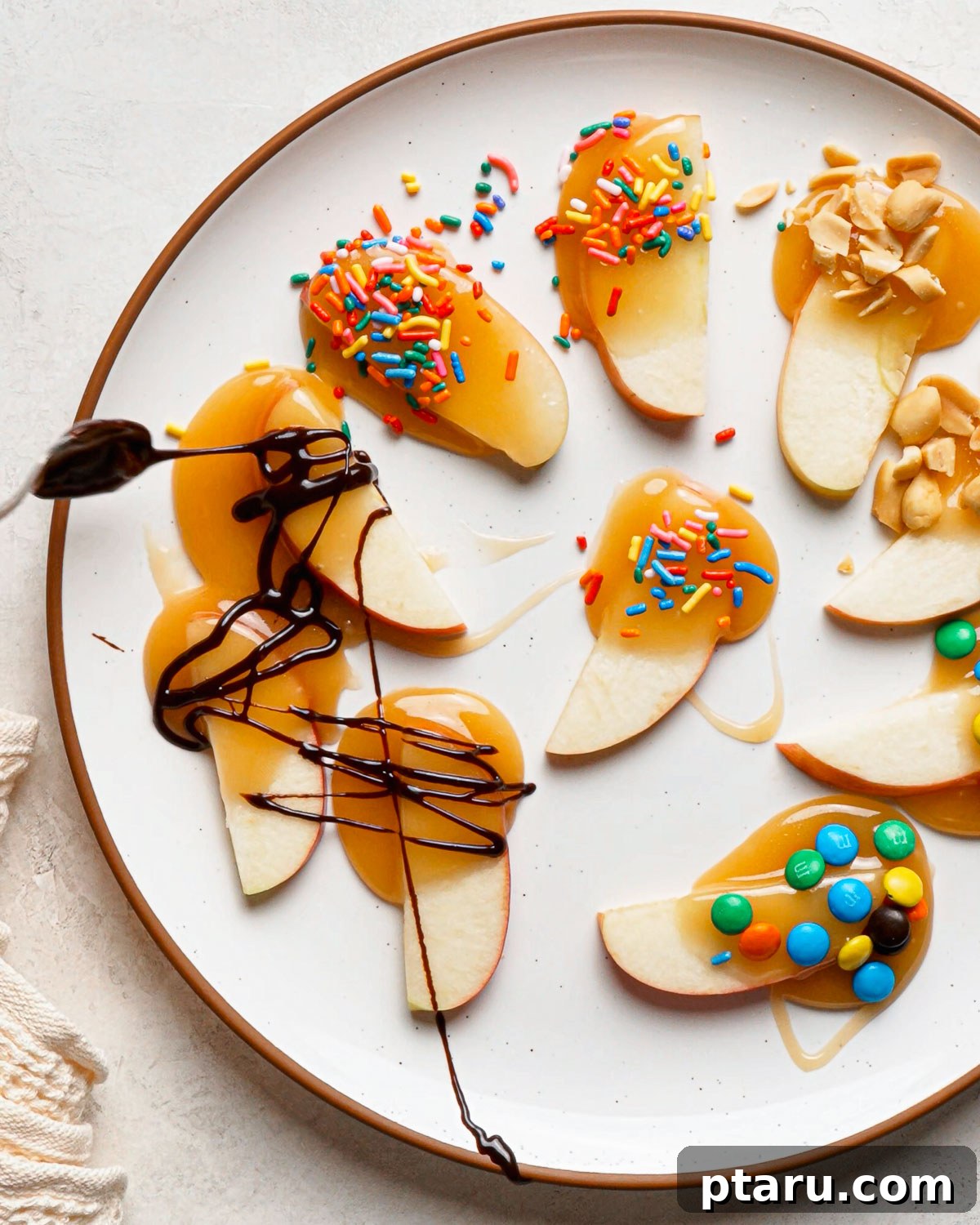 Caramel Apple Slices with Homemade Caramel Sauce 10 Caramel dipped apple slices with sprinkles, peanuts and mini M&M’s on a white plate.