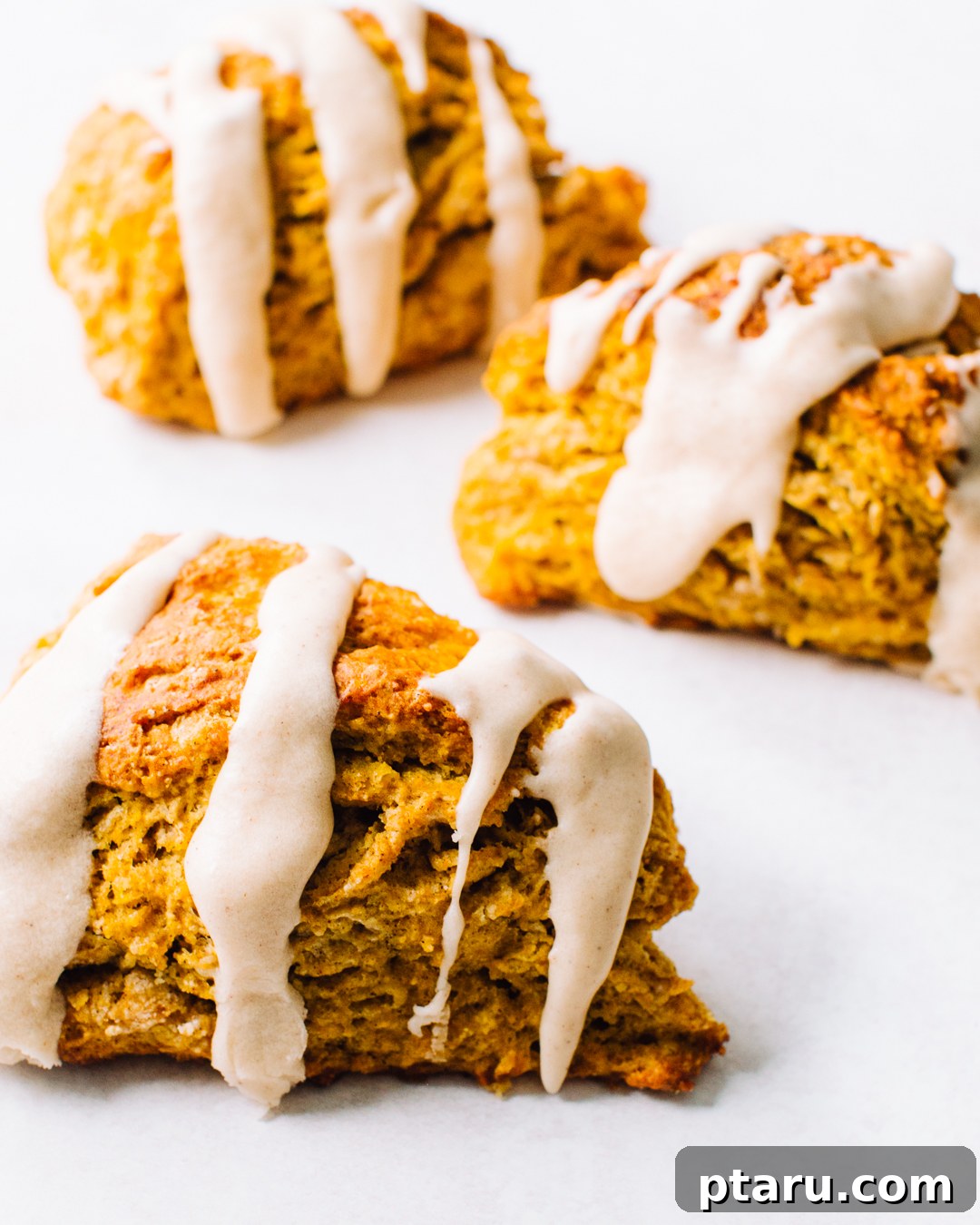 Soft Pumpkin Scones Recipe with Cinnamon Glaze 2 Pumpkin scones drizzled with cinnamon glaze on a white background.