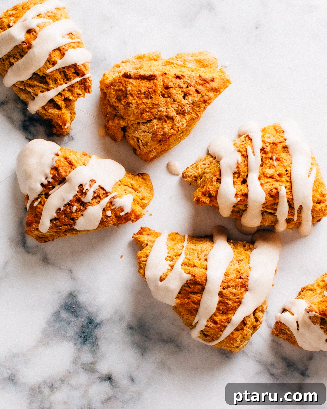 Soft Pumpkin Scones Recipe with Cinnamon Glaze 8 Pumpkin scones with cinnamon glaze on a marble surface.