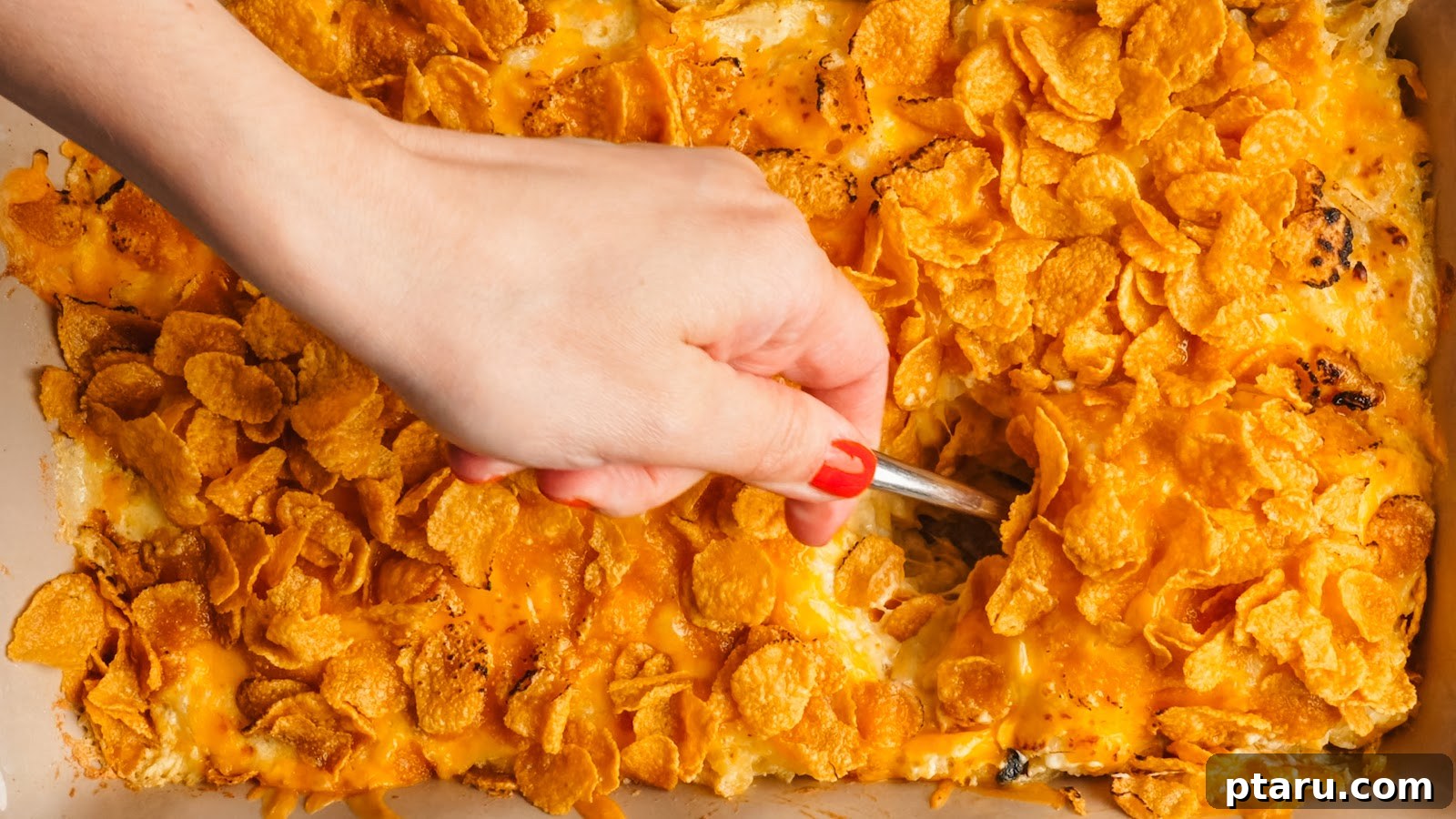 Funeral Potatoes: Cheesy Casserole with Cornflake Topping 12 Scooping a serving of cheesy potato casserole from the baking dish.