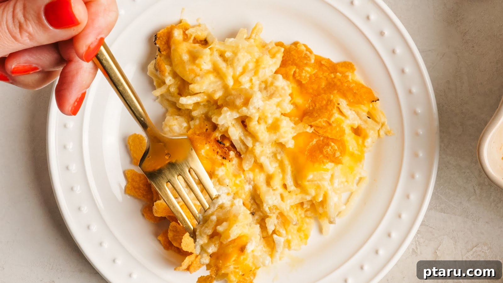 Funeral Potatoes: Cheesy Casserole with Cornflake Topping 14 A plated serving of cheesy potato casserole with a fork.