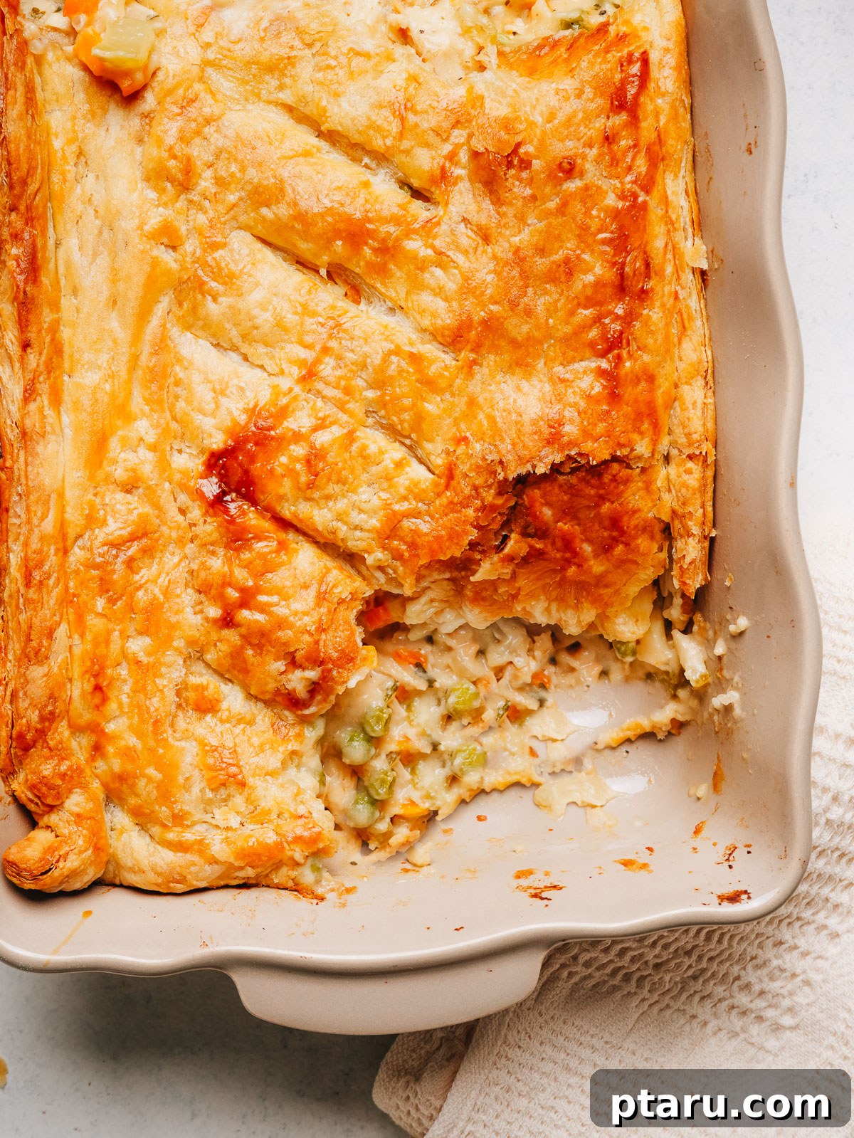 Creamy Chicken Pot Pie Casserole with Flaky Puff Pastry 2 Chicken pot pie casserole in a white baking dish with a serving scooped out of the golden puff pastry crust.