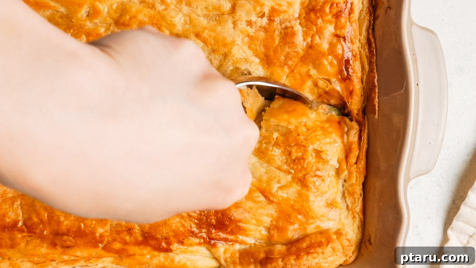 Creamy Chicken Pot Pie Casserole with Flaky Puff Pastry 15 Lifting a portion of golden puff pastry from a chicken pot pie casserole.