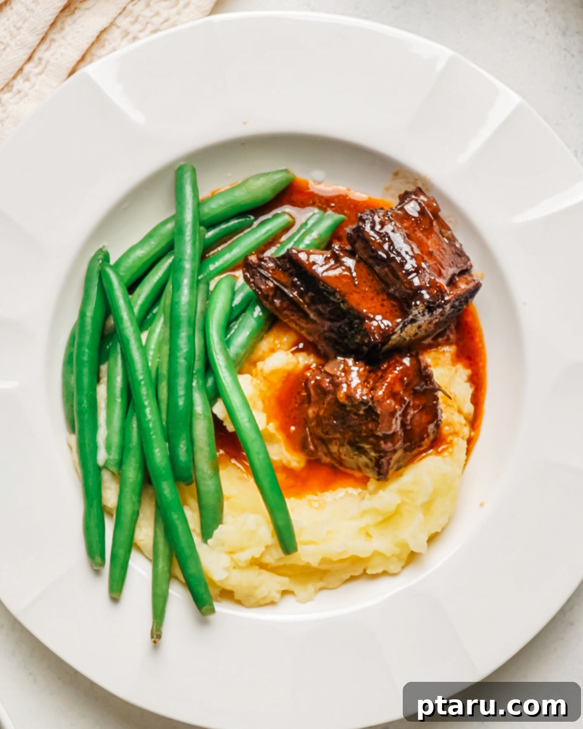Red Wine-Braised Beef Short Ribs That Fall Apart 12 Braised beef short ribs with mashed potatoes and green beans in a white bowl.
