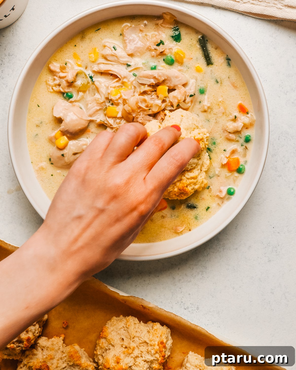 Slow Cooker Chicken Pot Pie with Drop Biscuits 11 A hand placing a buttermilk drop biscuit on a bowl of crockpot chicken pot pie.