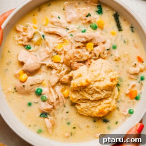 Crock pot chicken pot pie in a white bowl topped with a golden buttermilk drop biscuit.