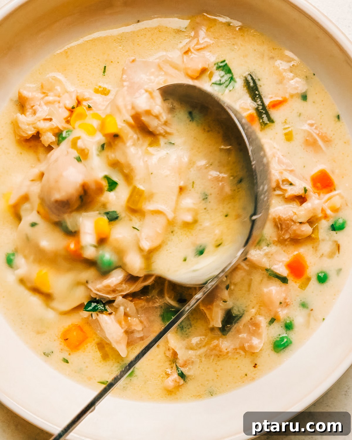 Slow Cooker Chicken Pot Pie with Drop Biscuits 10 A ladle scooping creamy slow cooker chicken pot pie filling with peas and carrots.