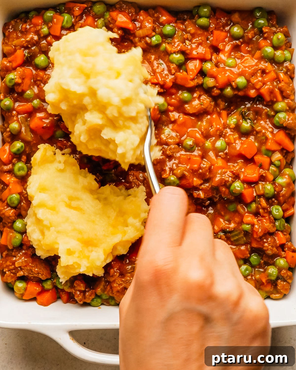 Classic Shepherd's Pie with Ground Beef or Lamb 14 Spooning mashed potatoes over shepherd's pie filling in a baking dish.