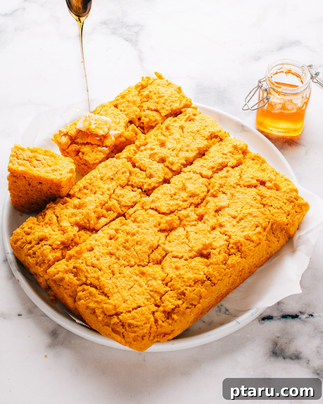 How to Make Moist Sweet Potato Cornbread 8 Sweet potato cornbread cut into squares on a white plate with honey drizzled over the top.