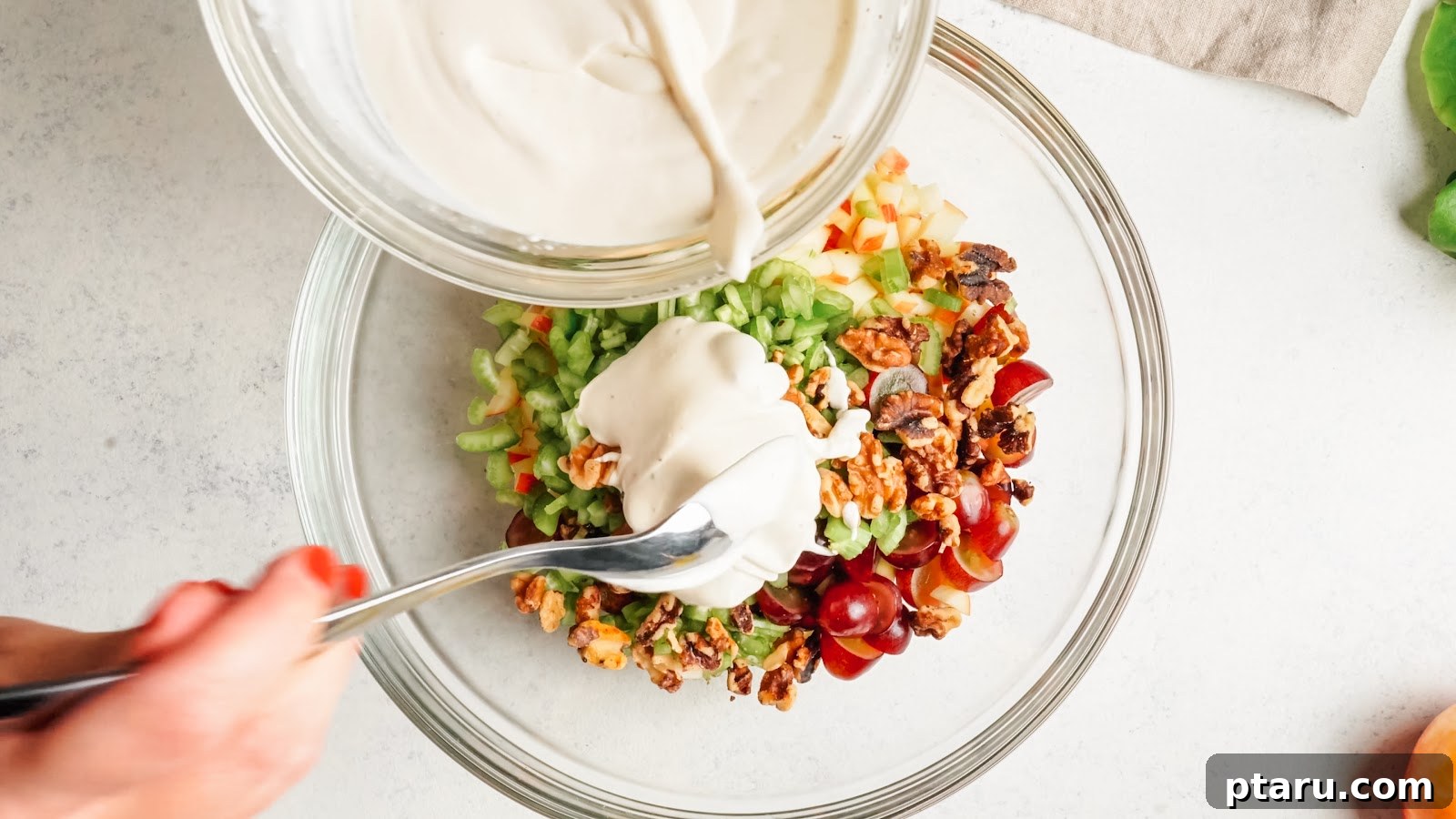 Classic Waldorf Salad with Apples, Grapes, and Walnuts 7 Pouring the creamy dressing over apples, celery, grapes and walnuts for classic creamy apple salad.