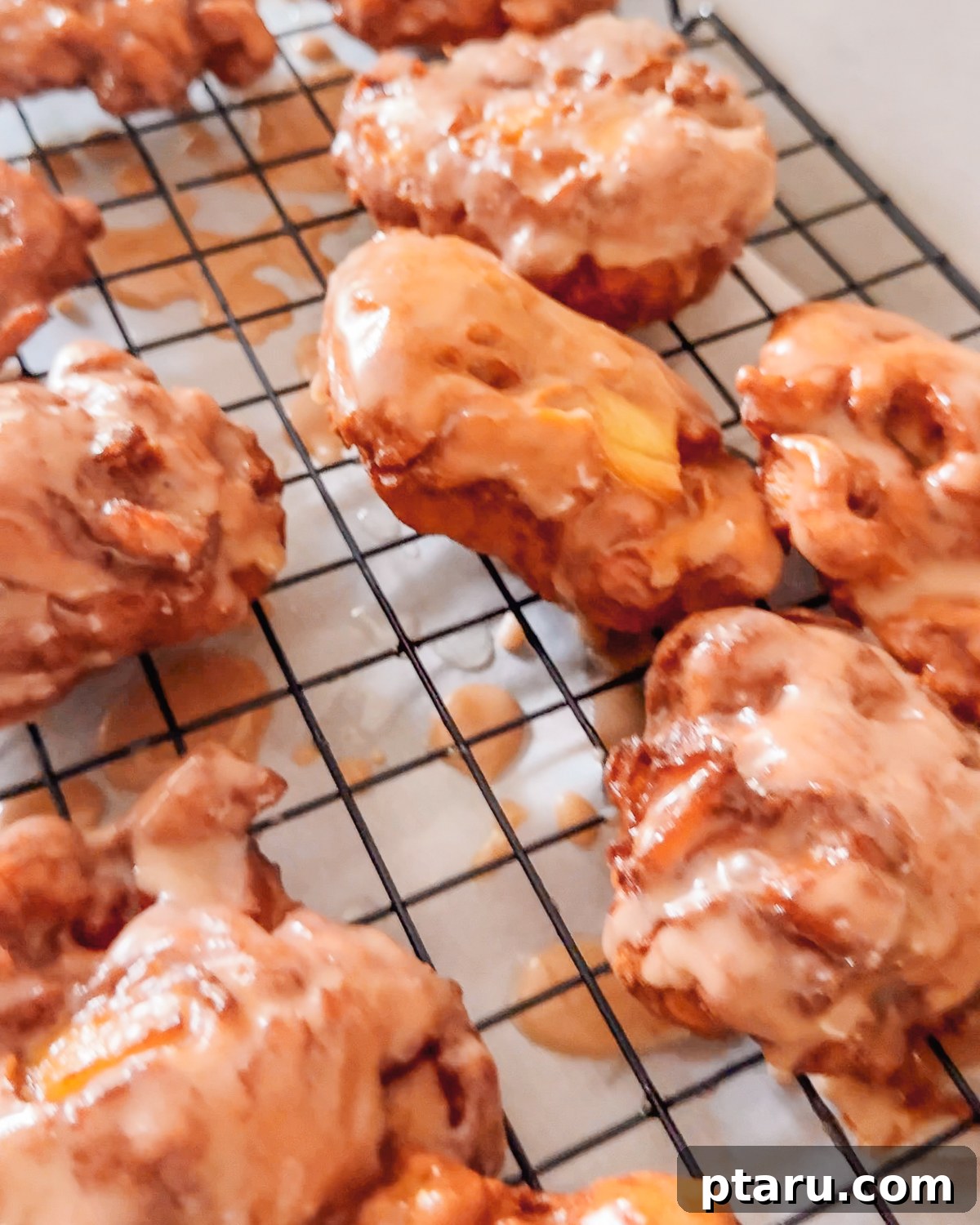 Crispy Homemade Apple Fritters with Cinnamon Glaze 10 Glazed apple fritters setting on a wire rack.
